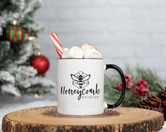 May include: A white ceramic mug with a black handle and rim, featuring a black graphic of a bee inside a hexagon above the text Honeycomb MOCKUPS. The mug is filled with white marshmallows and a red and white striped candy cane.