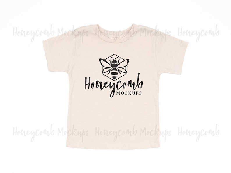 Op de afbeelding: Een beige baby-T-shirt met een zwarte bij en honingraat-afbeelding en de tekst "Honeycomb Mockups".