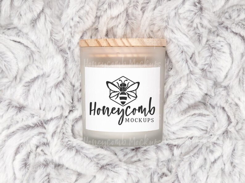 May include: A frosted glass candle jar with a wooden lid and a white label. The label has a black and white illustration of a bee in a honeycomb and the text "Honeycomb Mockups".