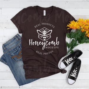 May include: A brown t-shirt with a white honeycomb design and the text "Real Products, Honeycomb Mockups, Real Photos". The shirt is laid flat on a white wooden surface with a pair of black canvas shoes and a bouquet of yellow sunflowers.
