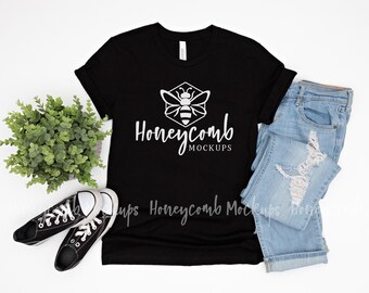 Puede incluir: Una camiseta negra de manga corta con un gráfico blanco de una abeja dentro de un hexágono y el texto Honeycomb MOCKUPS, junto a unos vaqueros azul claro desgastados y zapatillas de lona bajas en blanco y negro.