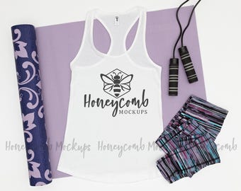 May include: A white racerback tank top featuring a black bee graphic inside a hexagon and the text Honeycomb MOCKUPS. The set includes a purple yoga mat with a floral pattern, a black jump rope, and patterned leggings with stripes.