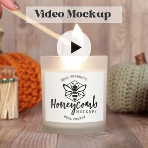 May include: A white candle with a black and white logo that says "Honeycomb Real Products Real Photos" is lit with a match. The candle is surrounded by knitted pumpkins.