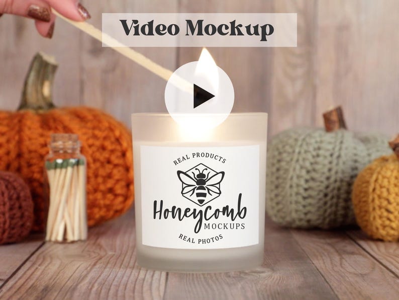 May include: A white candle with a black and white logo that says "Honeycomb Real Products Real Photos" is lit with a match. The candle is surrounded by knitted pumpkins.
