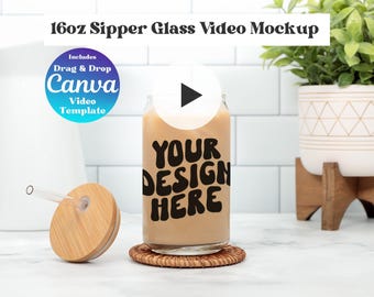 May include: A 16oz clear glass tumbler filled with a beige liquid, featuring the black text 'YOUR DESIGN HERE'. It includes a bamboo lid with a clear glass straw and a circular badge stating 'Includes Drag & Drop Canva Video Template'.