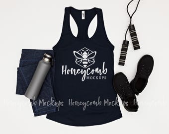 May include: A dark navy blue racerback tank top featuring a white graphic of a bee inside a hexagon with the text Honeycomb MOCKUPS, accompanied by dark blue leggings, a grey water bottle, black athletic shoes, and a black jump rope.
