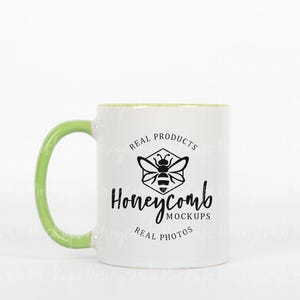 Pode incluir: Caneca de cerâmica branca com borda e alça verdes. A caneca tem um logotipo de abelha preto com o texto "Real Products Honeycomb Mockups Real Photos".