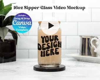 May include: A 16oz clear glass sipper with a bamboo lid, filled with a beige liquid. The glass features the black text 'YOUR DESIGN HERE' in a bold, wavy font. A circular play button icon is centred over the glass, and a blue badge reads 'Includes Drag & Drop Canva Video Template'.