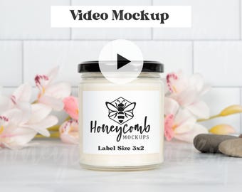 May include: A clear glass candle jar with a black lid and white wax. The label features a black bee icon inside a hexagon, the text Honeycomb MOCKUPS, and the text Label Size 3x2 inches. The candle is centered in the frame.