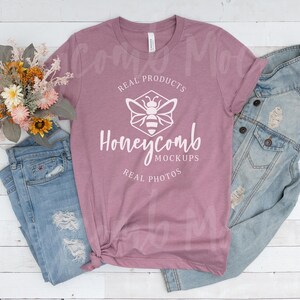 May include: A mauve t-shirt with the text "Honeycomb Mockups" and a bee graphic, paired with light blue denim jeans and a denim jacket. A bouquet of flowers rests on the side, creating a casual, lifestyle aesthetic.