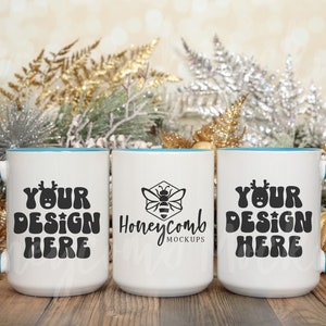 Puede incluir: Tres tazas de cerámica blanca con bordes y asas azules. Las tazas están dispuestas en fila sobre una superficie de madera. La taza del medio tiene un logotipo de abeja negro y el texto "Honeycomb Mockups". Las tazas a cada lado tienen el texto "Your Design Here" con un gráfico de reno.