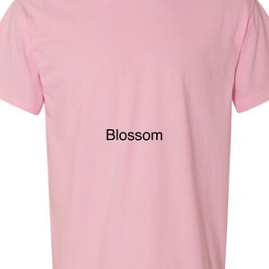 K&ouml;nnte beinhalten: Ein einfarbiges rosa T-Shirt mit dem Wort "Blossom" auf der Vorderseite.