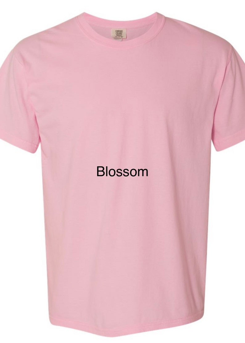 K&ouml;nnte beinhalten: Ein einfarbiges rosa T-Shirt mit dem Wort "Blossom" auf der Vorderseite.