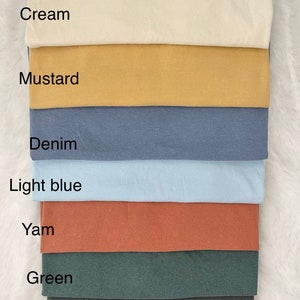 K&ouml;nnte beinhalten: Ein Stapel Stoffmuster in verschiedenen Farben, darunter Creme, Senf, Denim, Hellblau, Yam, Gr&uuml;n und Anthrazit.