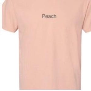 K&ouml;nnte beinhalten: Drei T-Shirts in verschiedenen Farben:  Kirschrot, Pfirsich und staubiges Blau. Jedes Shirt hat ein einzelnes Wort in schwarzer Schrift auf der Vorderseite gedruckt: "Crimson", "Peach" und "Dusty blue".