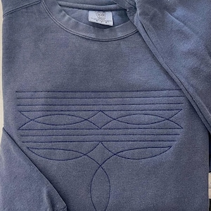 Puede incluir: Una sudadera azul oscuro con un dise&ntilde;o geom&eacute;trico bordado en la parte delantera. El dise&ntilde;o presenta una serie de l&iacute;neas curvas y diamantes, creando un patr&oacute;n sim&eacute;trico. La sudadera tiene cuello redondo y mangas largas.