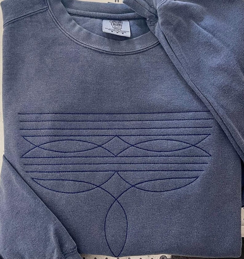 Puede incluir: Una sudadera azul oscuro con un dise&ntilde;o geom&eacute;trico bordado en la parte delantera. El dise&ntilde;o presenta una serie de l&iacute;neas curvas y diamantes, creando un patr&oacute;n sim&eacute;trico. La sudadera tiene cuello redondo y mangas largas.