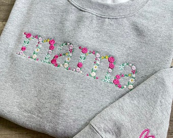 May include: Gray sweatshirt with the word "Mama" embroidered in pink and white flowers. A pink heart is embroidered on the sleeve.