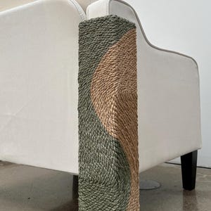 May include: A close-up of a couch armrest with a green and tan woven fabric protector. The protector is designed to prevent scratches and wear on the armrest.