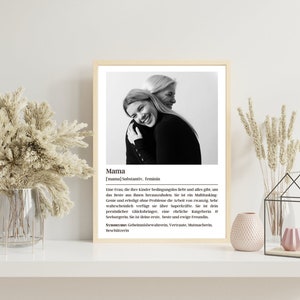 May include: Black and white photo of two women hugging. The photo is framed and has a definition of the word "Mama" in German below the photo. The definition describes a mother as a woman who loves her children unconditionally and gives everything to help them succeed. The definition also describes a mother as a multitasking genius who can do the work of twenty people.