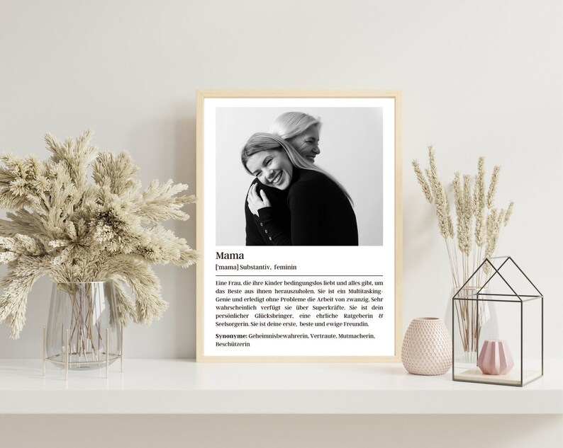 May include: Black and white photo of two women hugging. The photo is framed and has a definition of the word "Mama" in German below the photo. The definition describes a mother as a woman who loves her children unconditionally and gives everything to help them succeed. The definition also describes a mother as a multitasking genius who can do the work of twenty people.