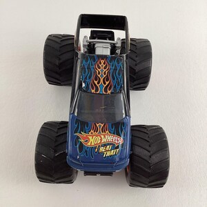 Puede incluir: Un juguete de cami&oacute;n monstruo Hot Wheels negro y azul con neum&aacute;ticos negros grandes. El cami&oacute;n presenta un dise&ntilde;o de llamas en el cap&oacute; y el texto "Hot Wheels Beat That!"