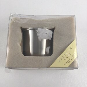 Könnte beinhalten: Ein silberner Babybecher in einer durchsichtigen Plastikbox mit einem gelben Etikett, auf dem "danforth baby handcrafted in vermont fine pewter" steht.