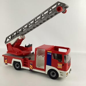 May include: A red and white toy fire truck with a gray extending ladder. The truck has black wheels and the number 112 and 122 are visible on the side. The ladder is extended upwards.