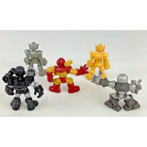 May include: A collection of five colorful toy robots. The robots are in various poses and colors, including red, yellow, gray, and black. The toys are made of plastic and have a cartoonish design.