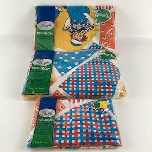 May include: Three packages of Pacific No-Iron fitted sheets with a red, white, and blue checkered pattern and a cartoon girl on the front. The packages are labeled "Pacific No-Iron" and "Juveniles".