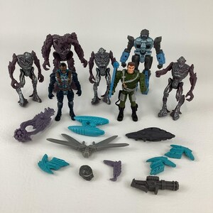 Peut inclure: Une collection de figurines et d'accessoires. Les figurines représentent des personnages humanoïdes de différentes couleurs, dont l'argent, le violet et le vert. Les accessoires comprennent un pistolet, un vaisseau spatial et d'autres éléments futuristes.