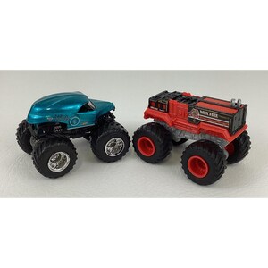 Pu&ograve; includere: Due monster truck giocattolo. Uno &egrave; verde acqua con ruote nere e la scritta "NEA 2000". L'altro &egrave; rosso con ruote nere e la scritta "MBX FIRE". Entrambi hanno pneumatici grandi e tassellati.