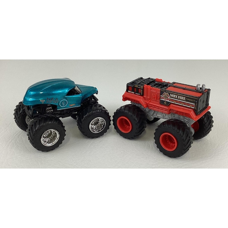 Pu&ograve; includere: Due monster truck giocattolo. Uno &egrave; verde acqua con ruote nere e la scritta "NEA 2000". L'altro &egrave; rosso con ruote nere e la scritta "MBX FIRE". Entrambi hanno pneumatici grandi e tassellati.