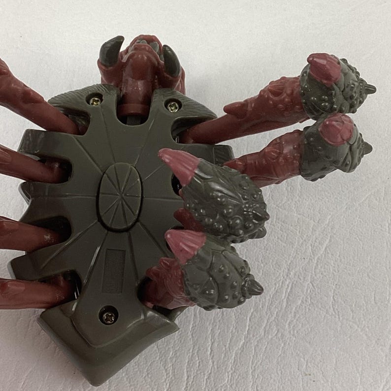 K&ouml;nnte beinhalten: Eine Actionfigur einer mehrbeinigen Kreatur mit einem dunkelgrauen Mittelk&ouml;rper und rotbraunen Gliedma&szlig;en. Die Gliedma&szlig;en haben texturierte, dunkelgraue, klauenartige Spitzen. Der Mittelk&ouml;rper ist mit sichtbaren Metallschrauben befestigt.