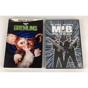 May include: Two DVD movie cases. The first is for "Gremlins" with a cartoon gremlin on the cover and the text "MONSTER MAYHEM!". The second is for "Men in Black" with two men in black suits holding guns and the text "M.I.B".