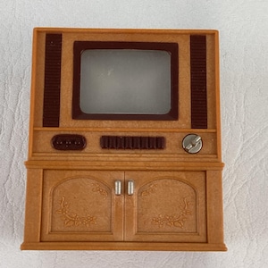 Op de afbeelding: Een miniatuur tv-toestel in vintage-stijl in bruin- en beigetinten. De tv heeft een rechthoekig scherm, een bedieningspaneel en een kast met twee deuren. Het ontwerp bevat decoratieve bloemmotieven.