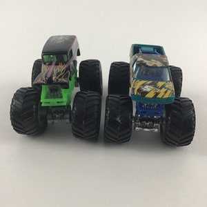 May include: Two monster trucks, one black with green flames and one green and yellow with a blue base, both with black tires.