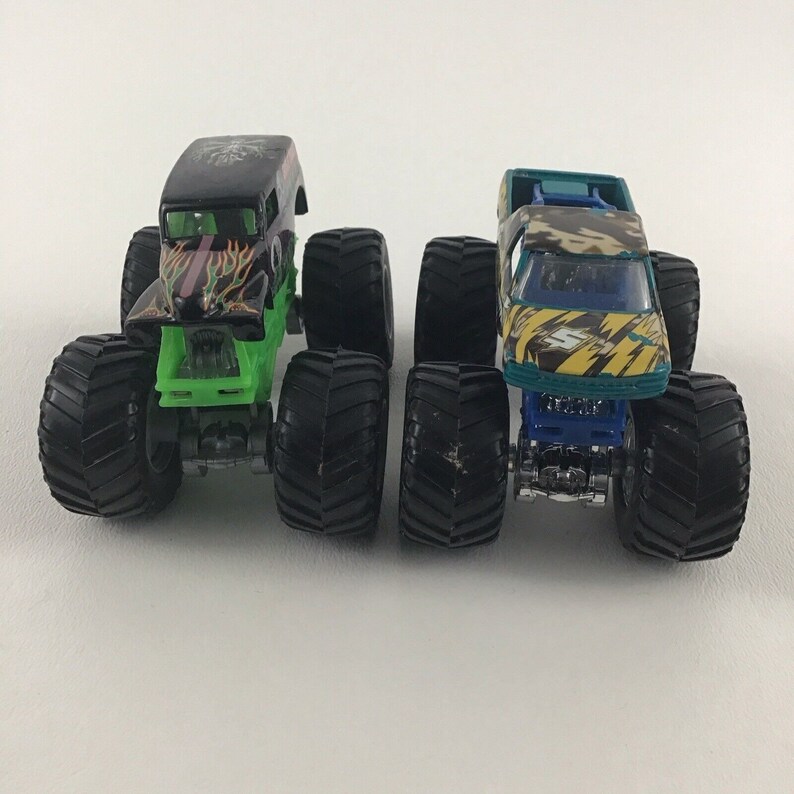May include: Two monster trucks, one black with green flames and one green and yellow with a blue base, both with black tires.