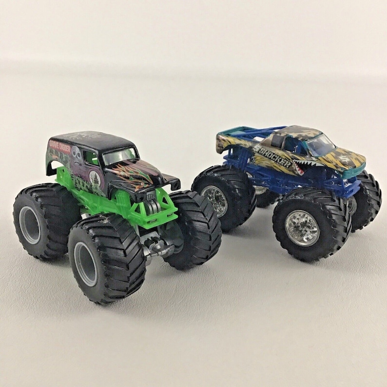 May include: Two monster truck toys, one green and black with "Grave Digger" written on the side, and the other blue and yellow with "Shockwave" written on the side.
