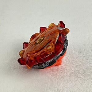 May include: A red, orange, and black toy with a circular design. The toy has a transparent orange top with red accents and a black and orange base. The toy is designed with a series of sharp, angular edges.