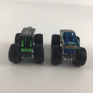 May include: Two monster trucks, one black with green accents and the words "Back To The Bone" on the side, and the other blue and green with a camouflage pattern.
