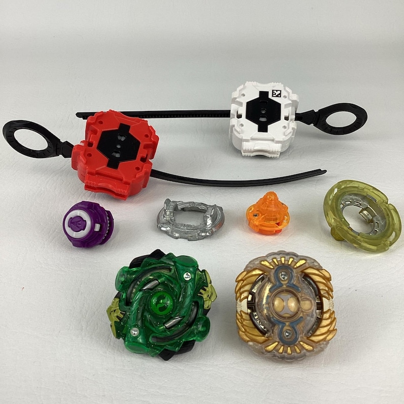 May include: A collection of colorful spinning top toys and launchers. The set includes various components in red, white, green, gold, orange, purple, and silver. The launchers have black pull strings.