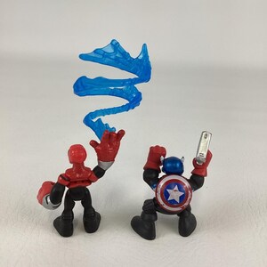 May include: Two action figures: one red and black figure with a silver gauntlet and a blue energy effect, and a Captain America figure with a shield and a silver device. The Captain America figure has a blue helmet and a shield with a white star.