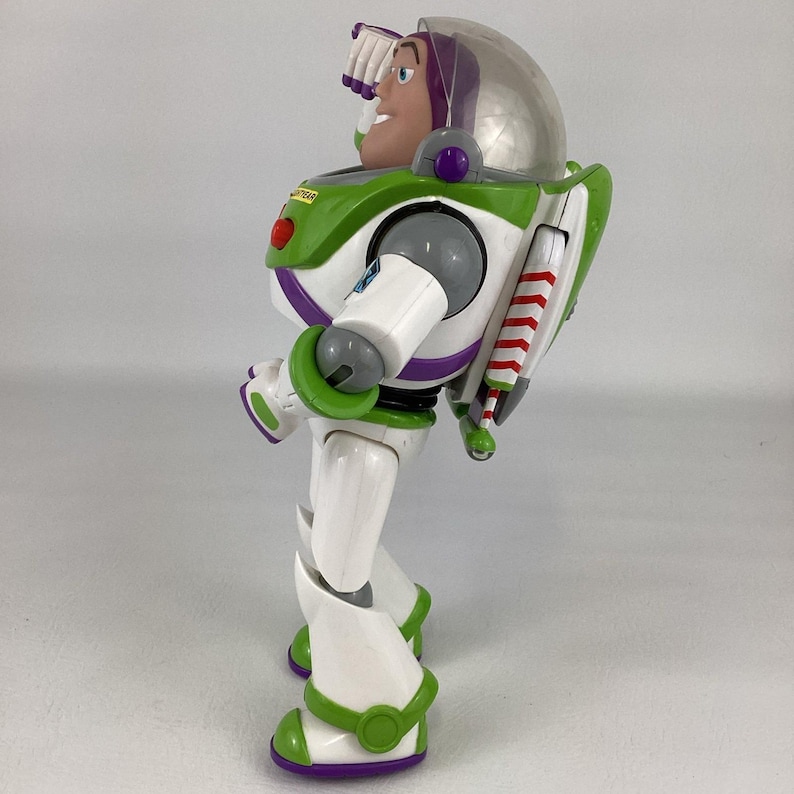 May include: A Buzz Lightyear action figure, featuring a white and green spacesuit with purple accents. The figure has a clear helmet, a red chest button, and a jetpack with red and white stripes. The toy is a collectible item.