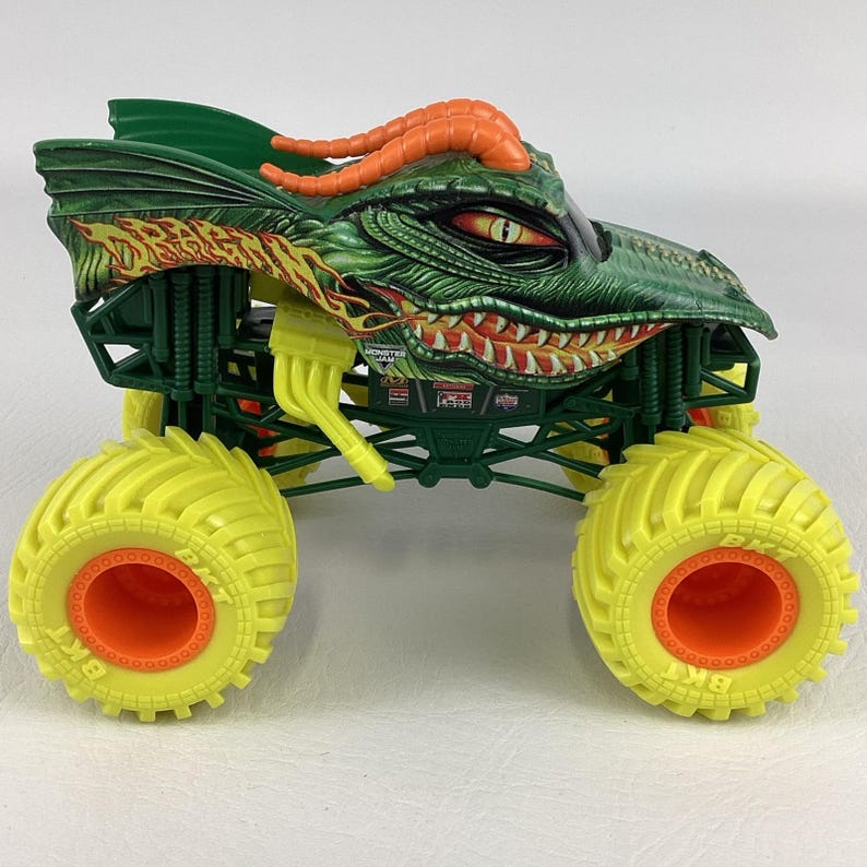 Pu&ograve; includere: Un giocattolo di monster truck verde e arancione con un design a testa di drago. Il camion ha grandi pneumatici gialli con centri arancioni e una carrozzeria verde dettagliata. La testa di drago presenta corna arancioni e un'espressione minacciosa.