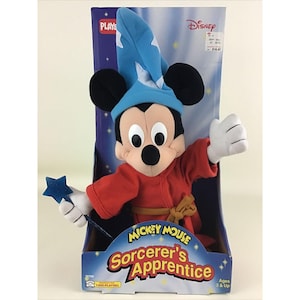 May include: A plush Mickey Mouse toy dressed as Sorcerer's Apprentice from the Disney movie Fantasia. He is wearing a blue hat, red robe, and holding a blue star-shaped wand. The packaging features the Disney logo and the words "Mickey Mouse Sorcerer's Apprentice".