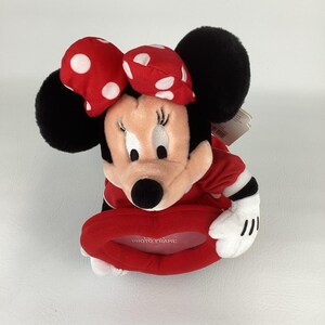 Pu&ograve; includere: Una cornice per foto di Minnie Mouse in peluche. La cornice &egrave; rossa a forma di cuore con la scritta "PHOTO FRAME". Minnie Mouse ha un fiocco rosso a pois bianchi, orecchie nere e un vestito rosso.