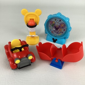 Pu&ograve; includere: Una collezione di giocattoli colorati a tema Mickey Mouse. Include un'auto rossa con sedile giallo, un canestro da basket giallo con palla, un orologio blu e un contenitore rosso con base blu.