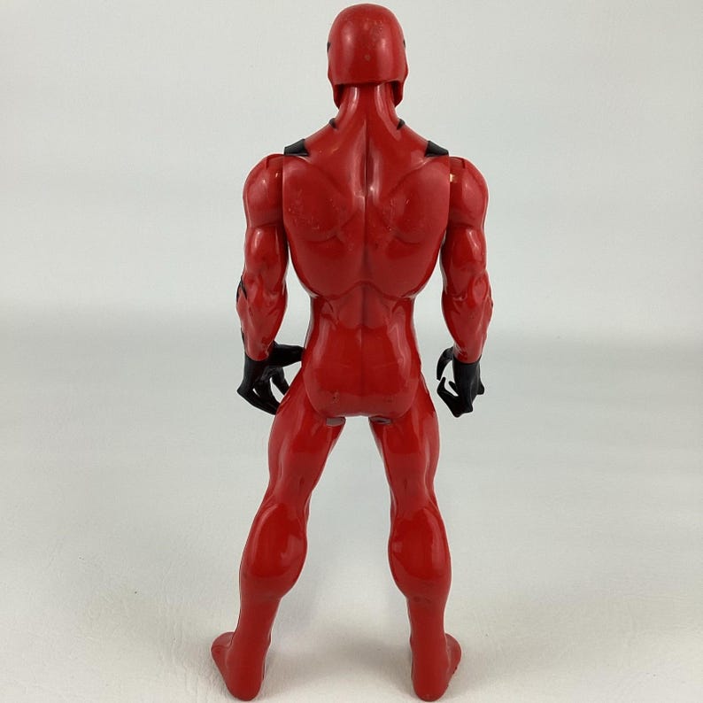 Puede incluir: Figura de acci&oacute;n roja de un superh&eacute;roe, vista desde atr&aacute;s. La figura tiene un f&iacute;sico musculoso, un casco y guantes negros. La figura est&aacute; de pie con las piernas separadas.