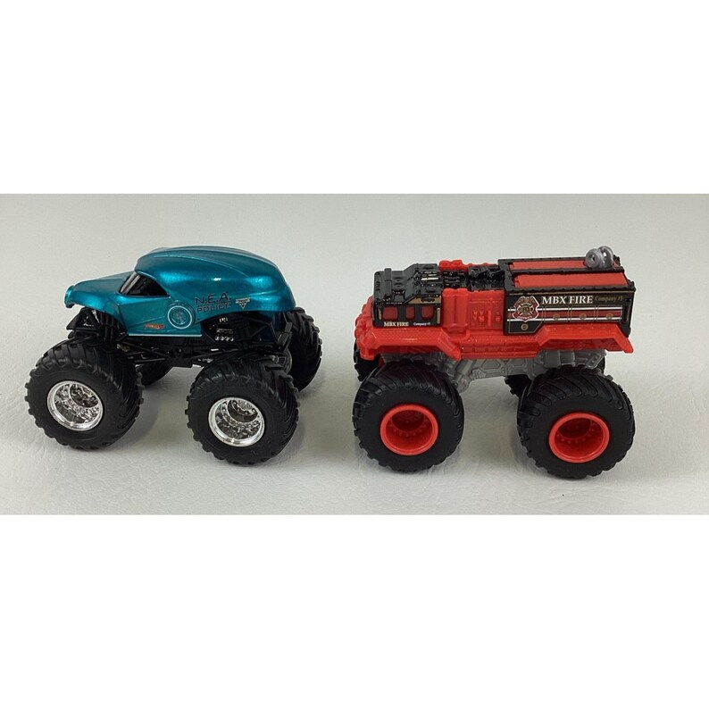 Pu&ograve; includere: Due monster truck giocattolo. Uno &egrave; verde acqua con ruote nere e cerchi argentati. L'altro &egrave; rosso con ruote nere e la scritta "MBX FIRE". Entrambi hanno pneumatici grandi e tassellati.